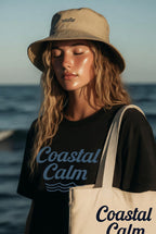 Woman wearing a 'Coastal Calm' shirt and tote bag with a beach background